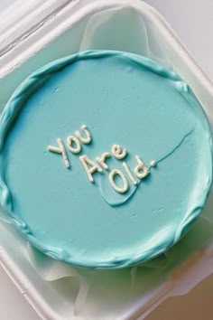 a blue cake with the words you are old written in frosting on it, sitting in a plastic container