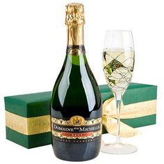 a bottle of champagne next to a wine glass with a gift box in the background