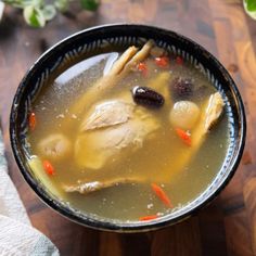 a black bowl filled with soup on top of a wooden table next to a napkin