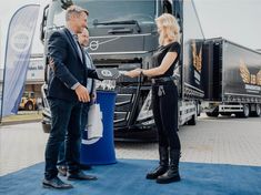 a man and woman shaking hands in front of a semi - truck at an event