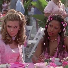 two women sitting at a table with pink flowers in their hair