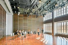 several people are sitting in chairs and talking to each other inside an empty room with large windows