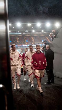 several men in red and white uniforms walking down a street at night with stadium lights behind them