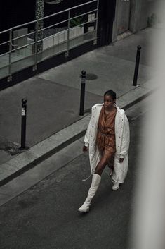 a woman is walking down the street wearing white boots and an overstuffed coat