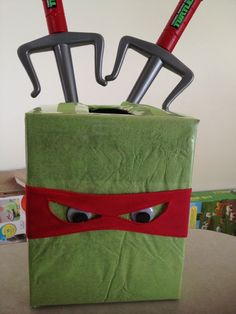 a green box with two ninja masks on it's face and some tools sticking out of the top