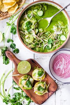 a bowl filled with green soup next to sliced radishes and cilantro