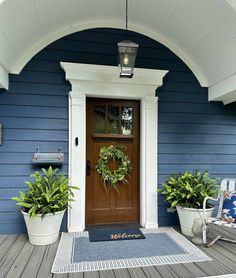 the front door is decorated with wreaths and two potted plants on the porch