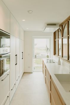 an empty kitchen with white counters and wooden cabinetry on the walls, along with a large window