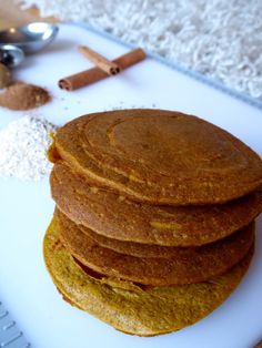 a stack of pancakes sitting on top of a white cutting board next to cinnamon sticks