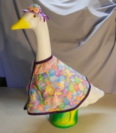 a white duck wearing a colorful dress on top of a green vase with a gray background