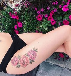 a woman laying on the ground with flowers tattooed on her stomach and arm, in front of some pink flowers