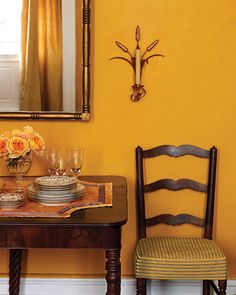 two chairs and a table with plates on it in front of a yellow wall,