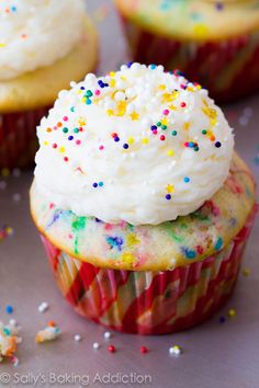 three cupcakes with white frosting and sprinkles on top are sitting next to each other