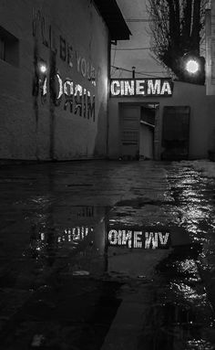 a black and white photo of a rainy night in front of a movie theater with neon lights