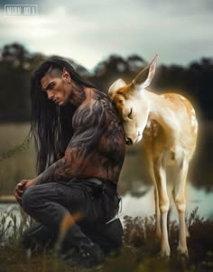 a man with long hair and tattoos sitting next to a small goat on the grass