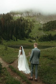 a bride and groom walking down a path in the mountains