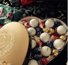 a heart shaped box filled with assorted golf balls next to a bag of chocolates