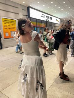 a woman in a white dress is talking on her cell phone while people are walking by