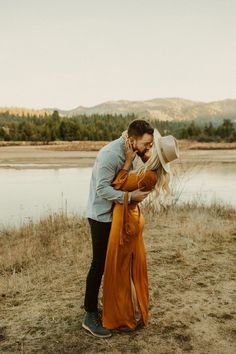 a man and woman standing next to each other in front of a body of water