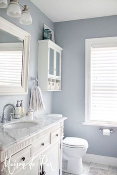 a white toilet sitting next to a sink in a bathroom under two large window shades