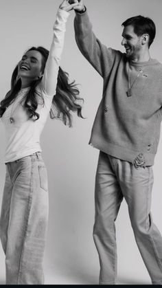 a man and woman dancing together with their arms in the air while wearing sweaters