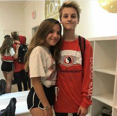 two young people standing next to each other in front of a book shelf with books on it