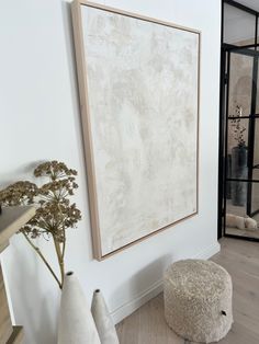 a painting hanging on the wall next to two vases and a round footstool