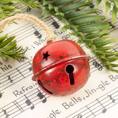 a red bell sitting on top of a sheet of music with green leaves around it