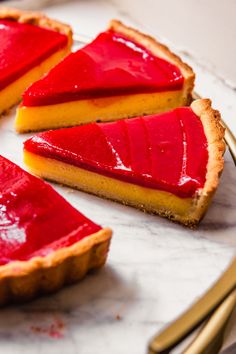 there is a piece of pie with red toppings on the plate next to gold utensils