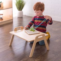 a little boy sitting on the floor playing with a wooden table and chair that he is using