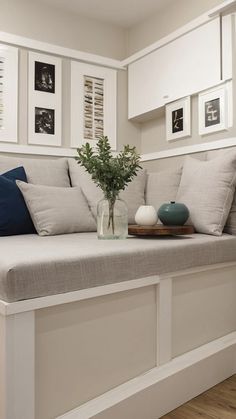 a white couch sitting next to a window with pictures on the wall behind it and a vase filled with flowers