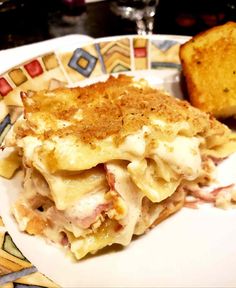 a white plate topped with lasagna next to a slice of toasted bread