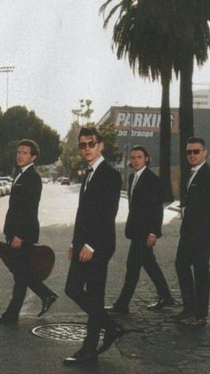 three men in suits and sunglasses are walking down the street with their guitar strings attached to their backs