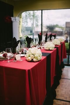 the table is set up with red cloths and white flowers on it, along with wine glasses