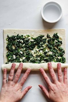 two hands on top of a pizza dough with spinach and fettuccine