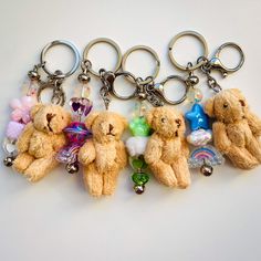 six teddy bears are arranged in a row on a white surface, one is holding a keychain