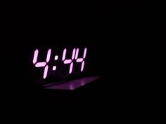 the digital clock is lit up in the dark with purple light on it's face