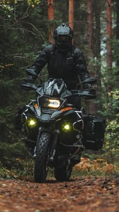 a man riding on the back of a motorcycle down a dirt road in the woods