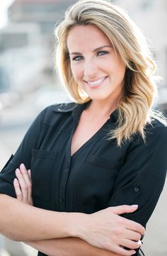 a woman with her arms crossed smiling at the camera while wearing a black shirt and jeans