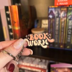 a person holding up a book worm sticker in front of bookshelves with other books behind them