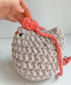 a hand is holding onto a small crocheted bag with a red bow on it