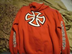 a red hoodie with white letters on it and a cross in the middle is laying on a bed