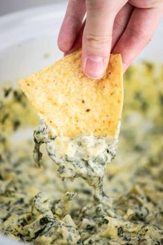 a tortilla chip being dipped with spinach and cheese in a white bowl