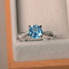 an engagement ring with a blue topazte surrounded by white diamonds in a wooden box