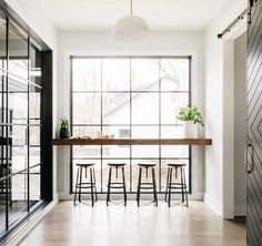 a kitchen with three stools next to a table and windows in the wall behind it