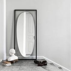 a mirror sitting on top of a floor next to a white busturine and shoes