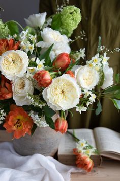 a vase filled with white and orange flowers next to an open book