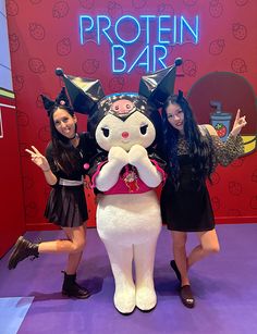 two girls standing next to a large stuffed animal in front of a sign that says protein bar