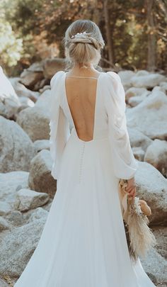 a woman in a wedding dress standing on rocks with her back turned to the camera