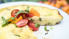 an omelet with tomatoes and basil on top is sitting on a white plate